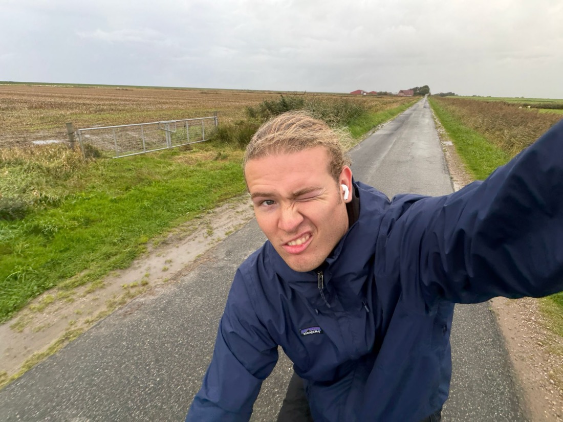 Zwinker-Selfie auf einer endlos geraden Landstraße unter grauem Himmel